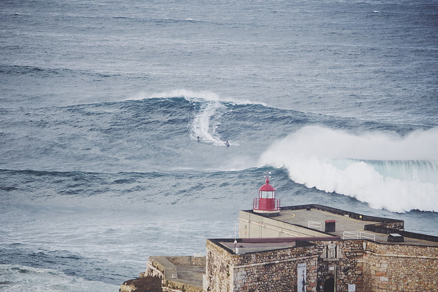 Surfers riding waves near historic lighthouse fortification