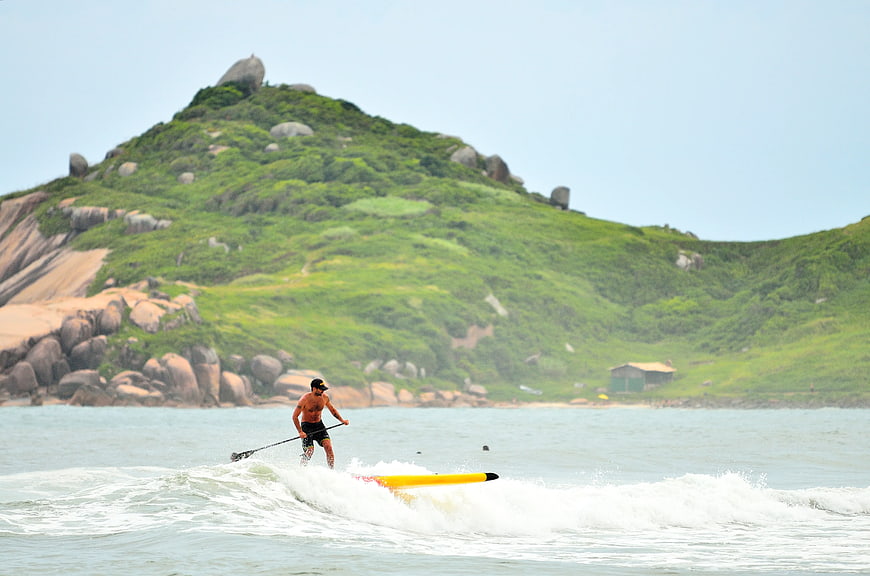 Man Stand Up Paddle Surfing on Wave with Green Island Background