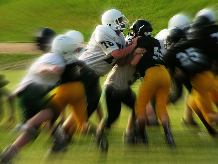 Action shot of youth football players tackling on grass field
