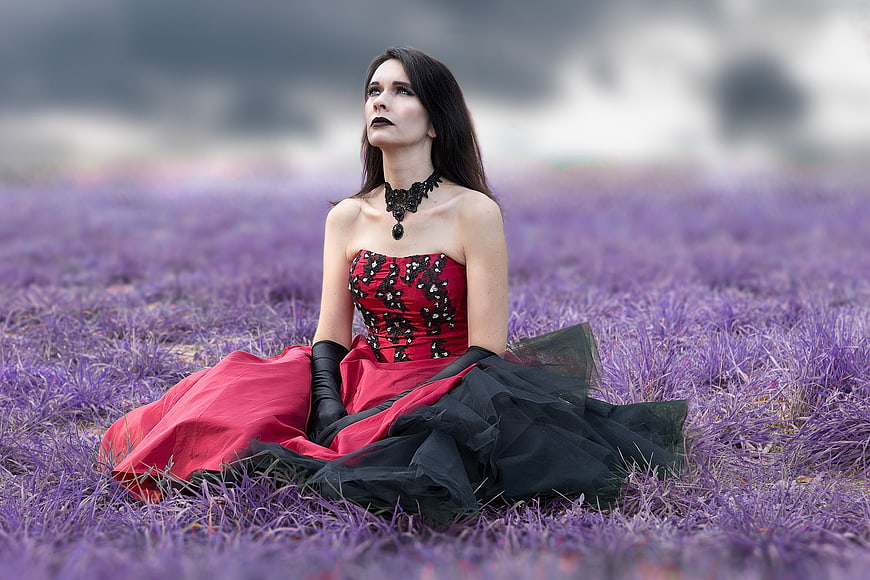Gothic woman in red and black dress sitting in purple field