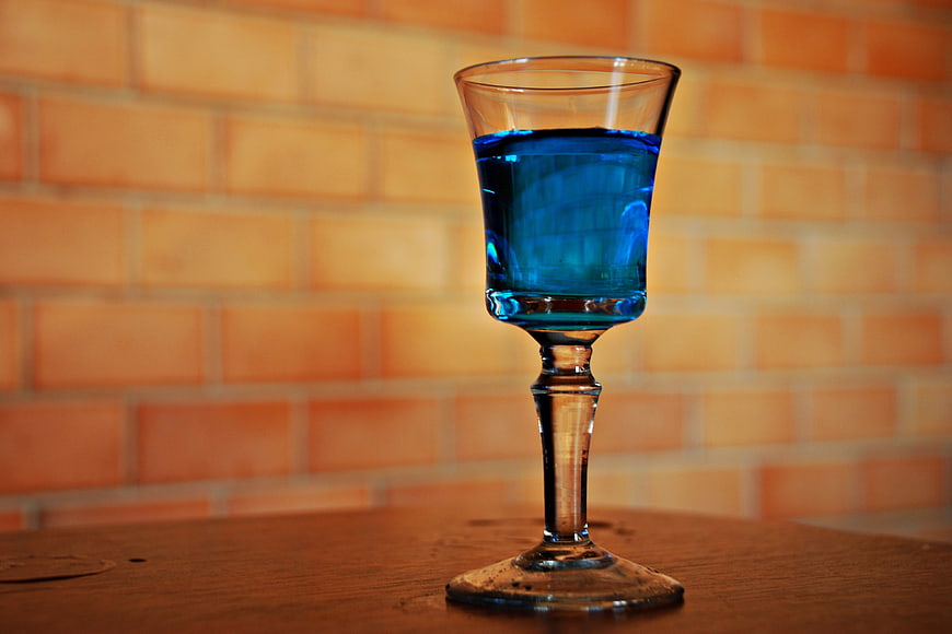 Blue cocktail in glass on wooden table with brick background