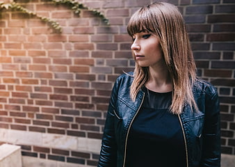 Woman in Leather Jacket Against Brick Wall