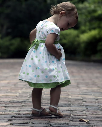 Toddler girl in polka dot dress walking on brick path