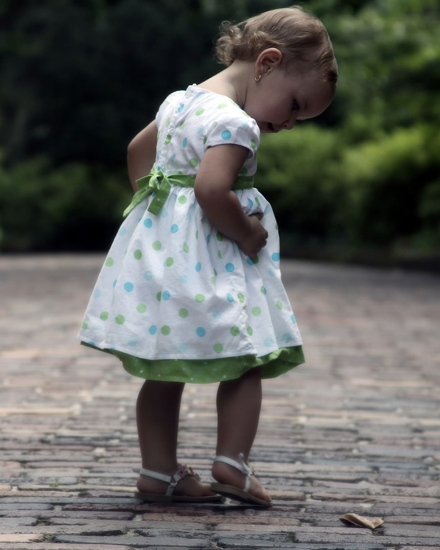 Toddler girl in polka dot dress walking on brick path