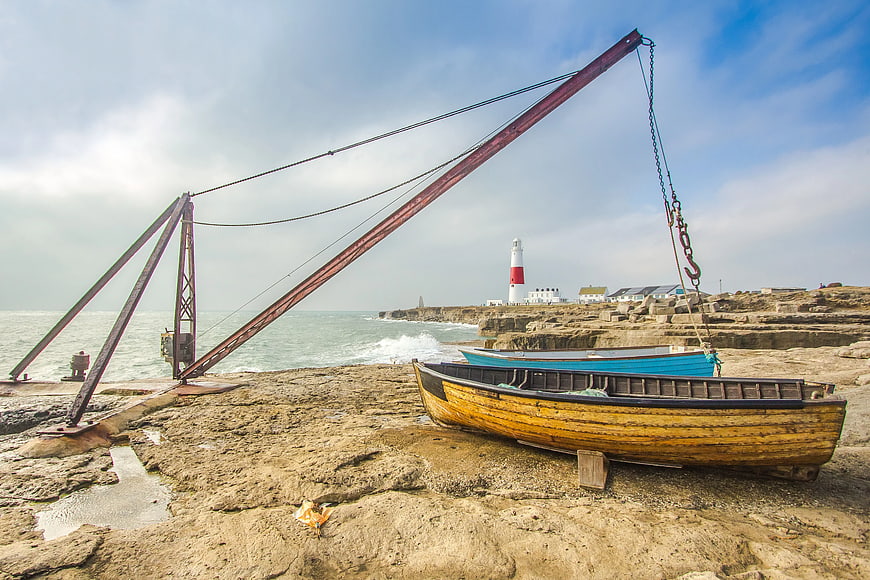 Rusty boat crane and wooden fishing boats on rocky coast