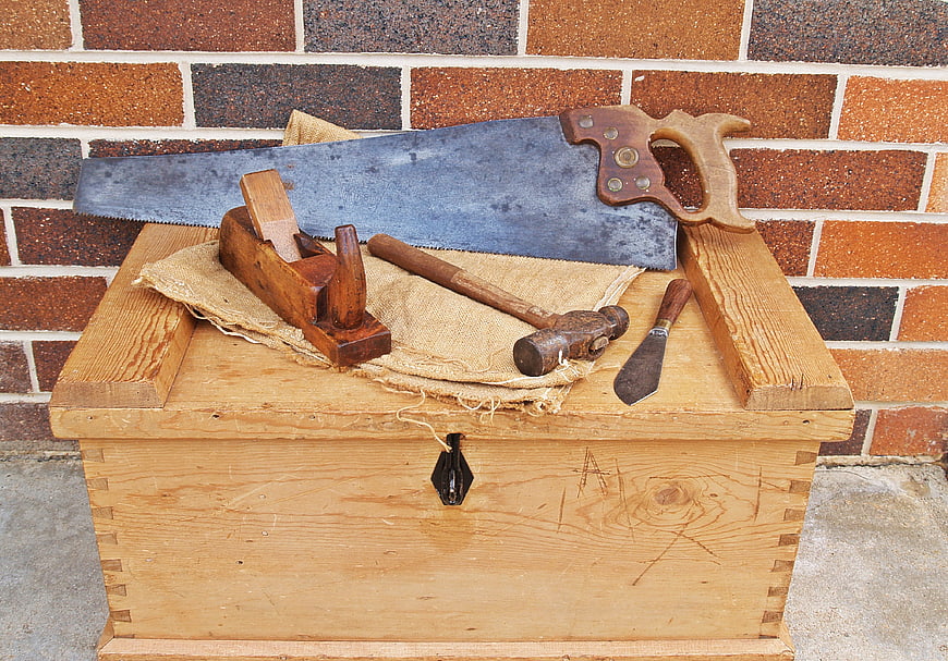 Vintage woodworking tools on wooden chest against brick wall