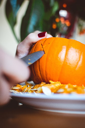 Close-up of hands carving a bright orange pumpkin for Halloween