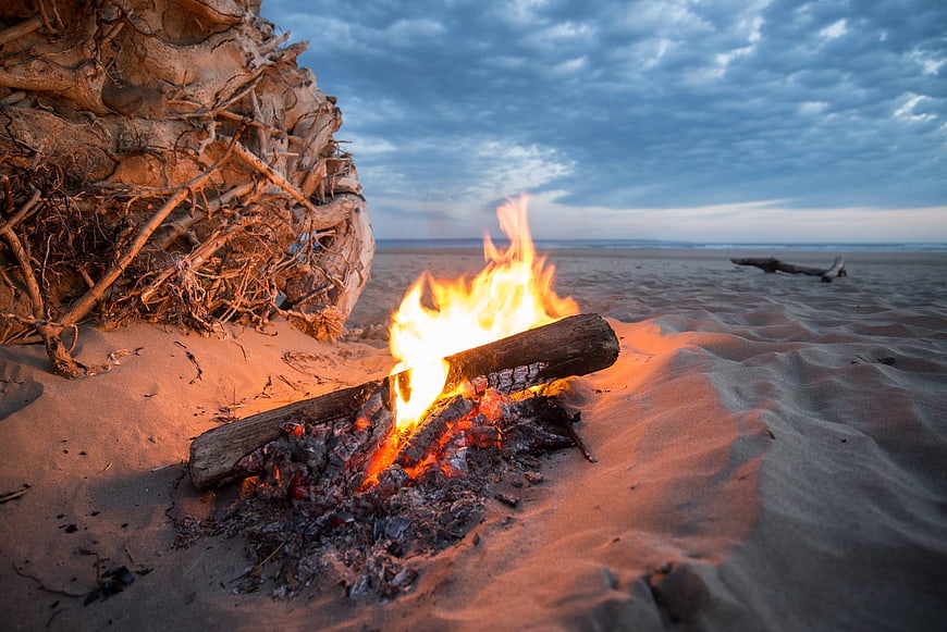 Campfire on Sandy Beach at Dusk with Driftwood