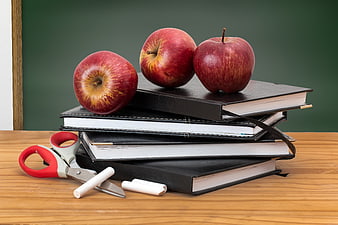 Stack of Books with Apples and Scissors on Wooden Desk