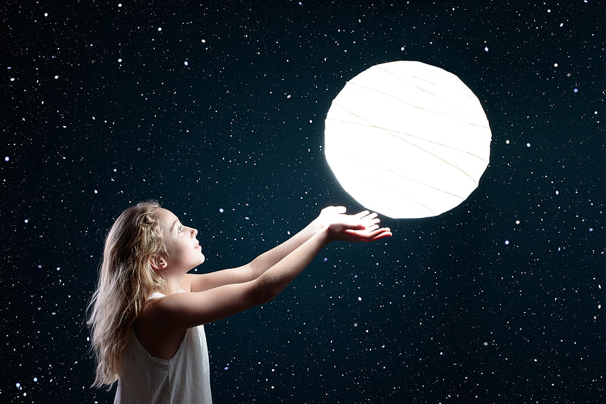 Young girl reaching for a glowing moon against a starry night sky