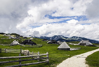 Traditional wooden huts in green mountain meadow with clouds