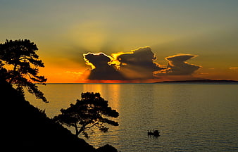Dramatic sunset over calm sea with silhouetted trees and boat