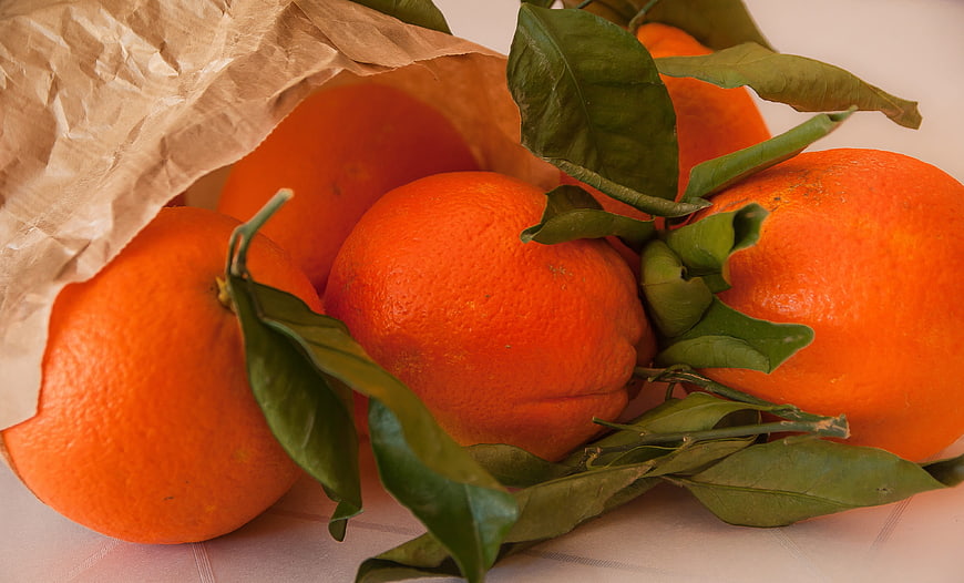 Fresh Oranges with Leaves Spilling from Brown Paper Bag
