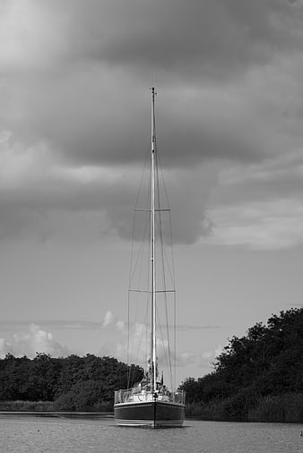 Black and white sailboat on calm water with cloudy sky