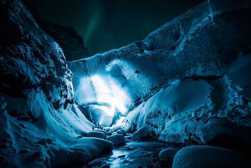 Blue Ice Cave Interior with Glowing Light and Snowy Rocks