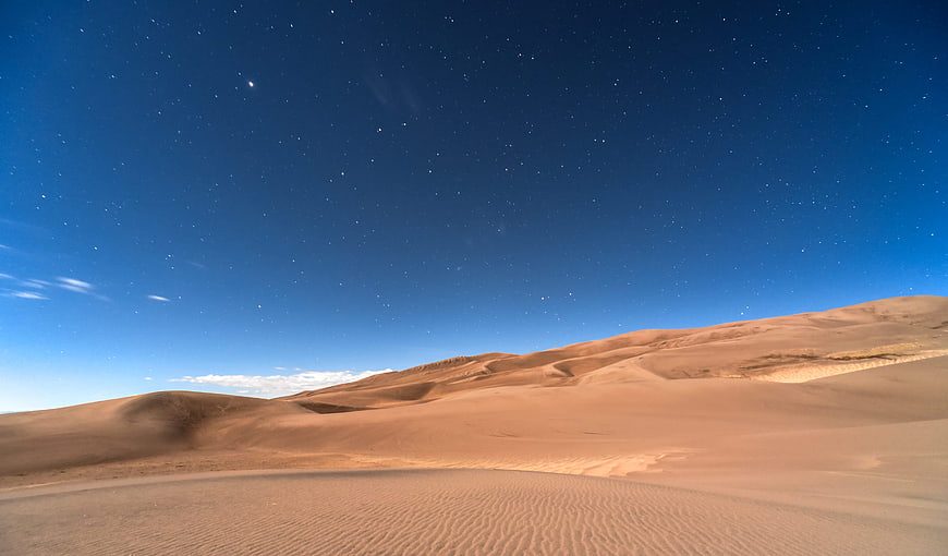 Starry Night Sky Over Golden Sand Dunes in Desert Landscape