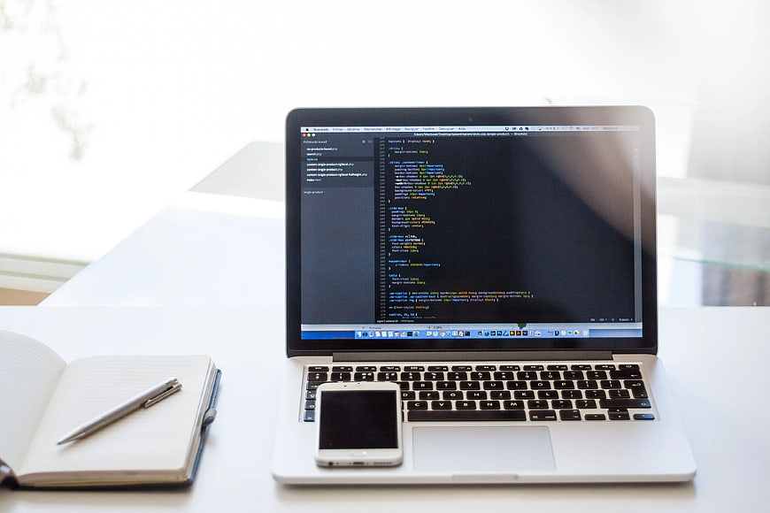 Laptop with code, smartphone, and notebook on white desk