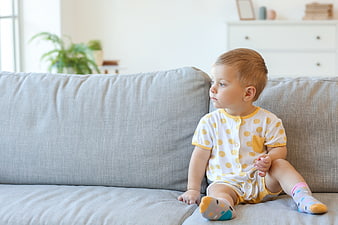 Toddler Boy Sitting on Gray Sofa in Bright Living Room