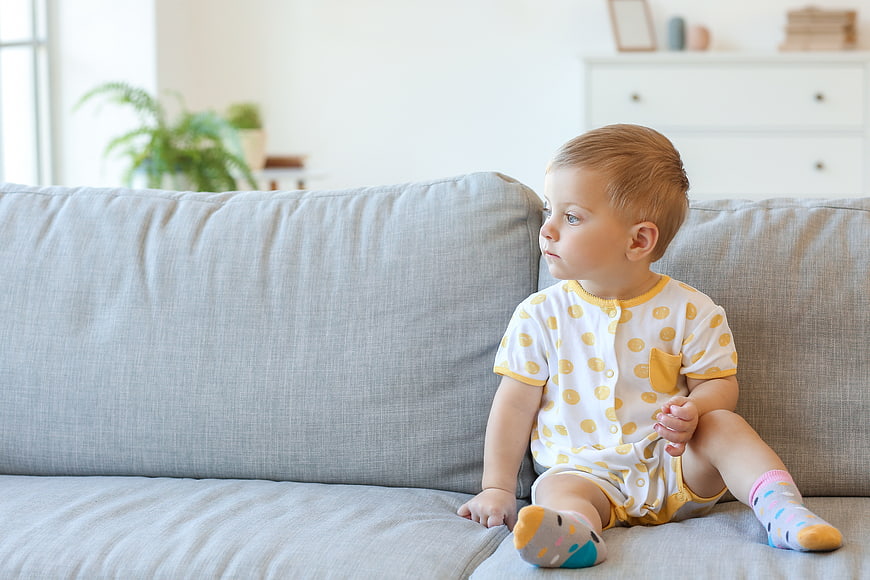 Toddler Boy Sitting on Gray Sofa in Bright Living Room