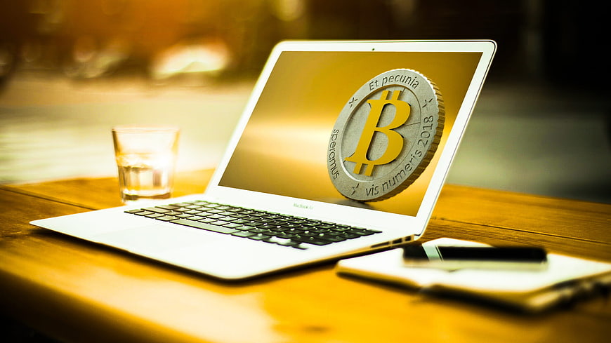 Bitcoin coin on laptop screen with smartphone and notepad on wooden desk