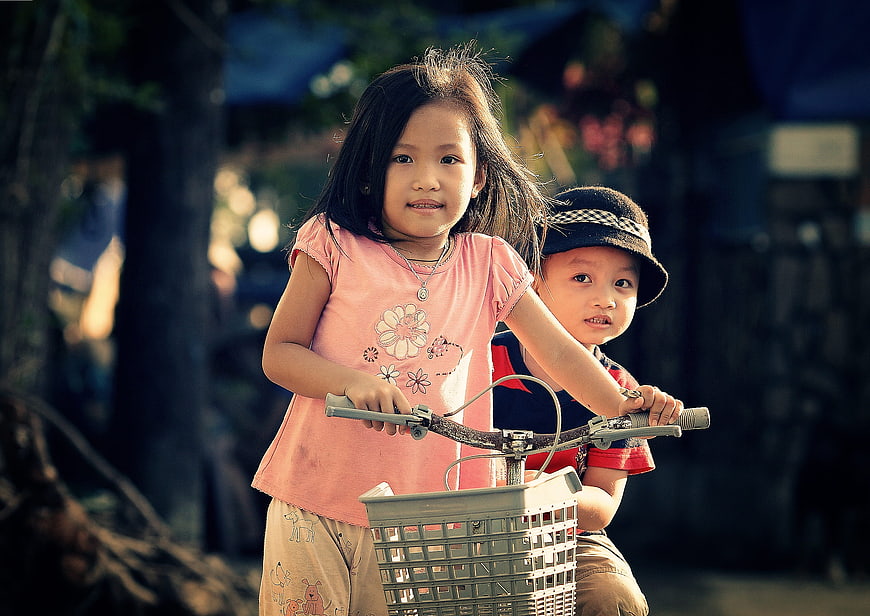 Two young children riding a bicycle together outdoors