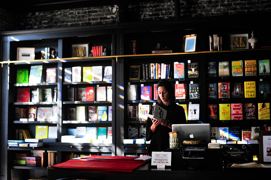 Woman Reading Book in Modern Bookstore with Sunlight