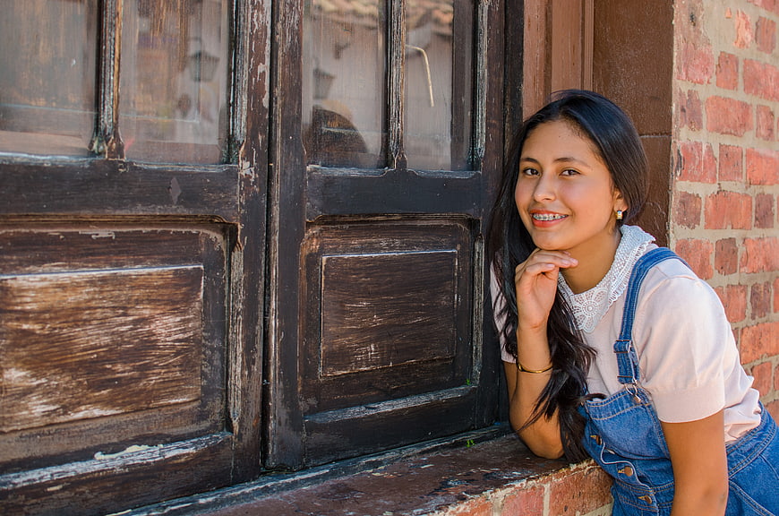Smiling young woman leaning against rustic wooden window