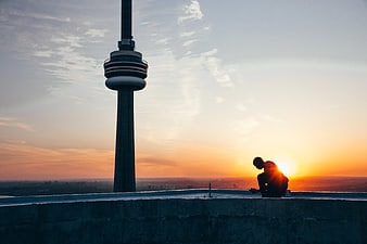 Man Silhouette Sitting on Rooftop with TV Tower at Sunset