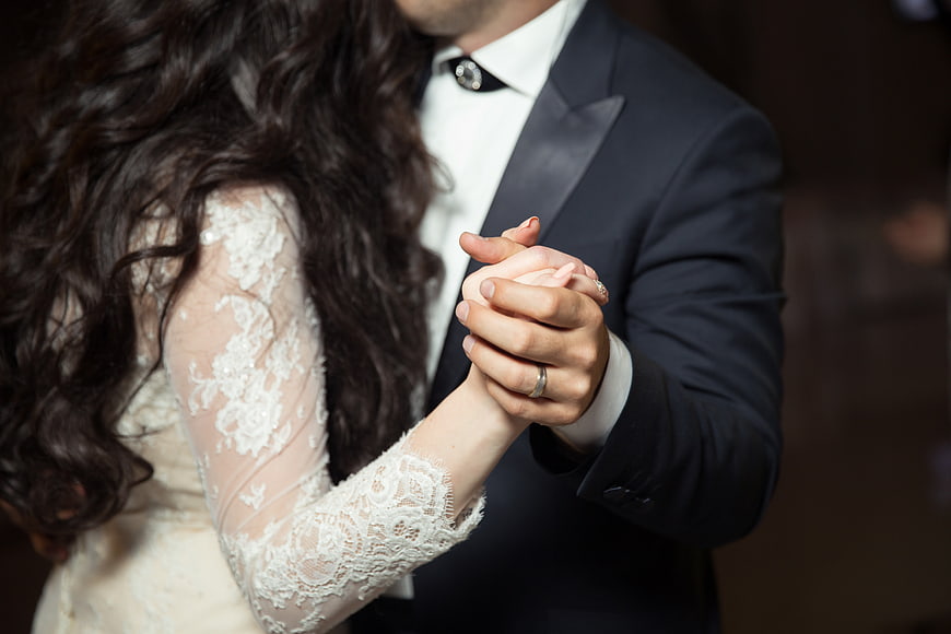 Close-up of bride and groom holding hands while dancing at wedding