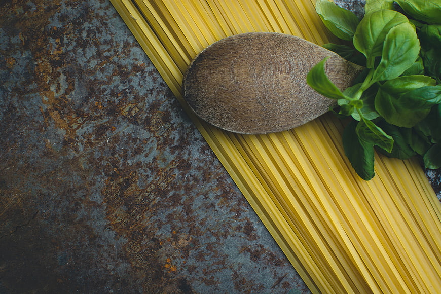 Uncooked spaghetti with basil and wooden spoon on rustic metal