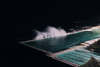 Ocean waves crashing into outdoor swimming pool at night
