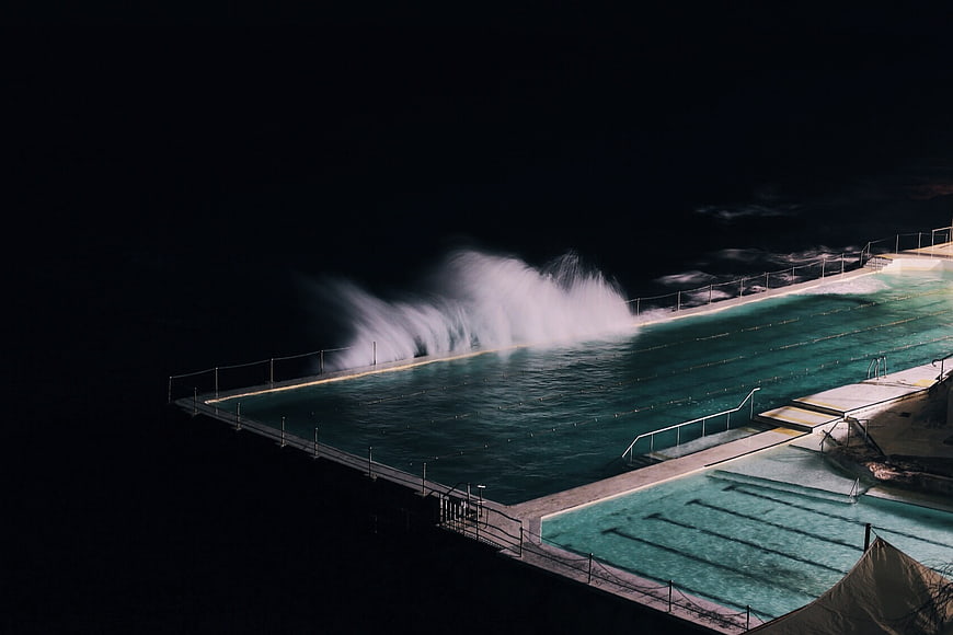 Ocean waves crashing into outdoor swimming pool at night