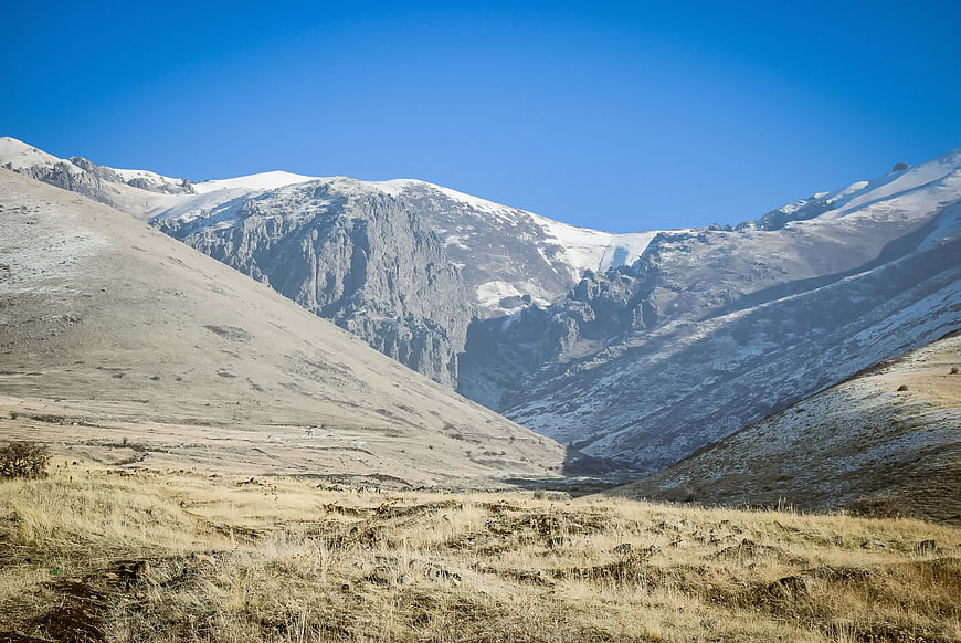 Snow-capped mountain range with dry grassy valley foreground