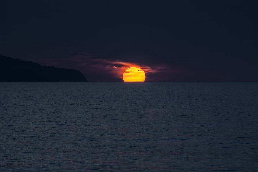 Dramatic orange sunset over dark ocean with silhouetted island