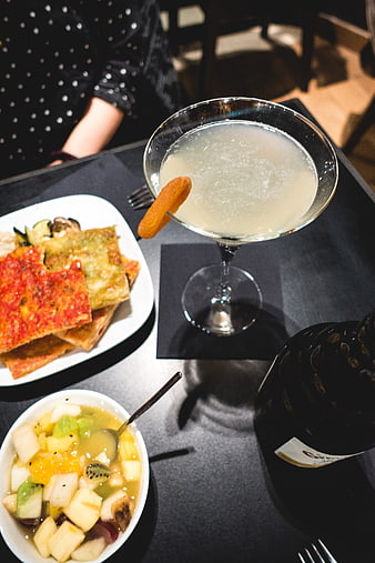 Cocktail with dried apricot, savory flatbread, and fruit salad on a dark table