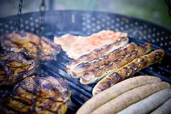 Grilled sausages and steaks on a barbecue grill with smoke