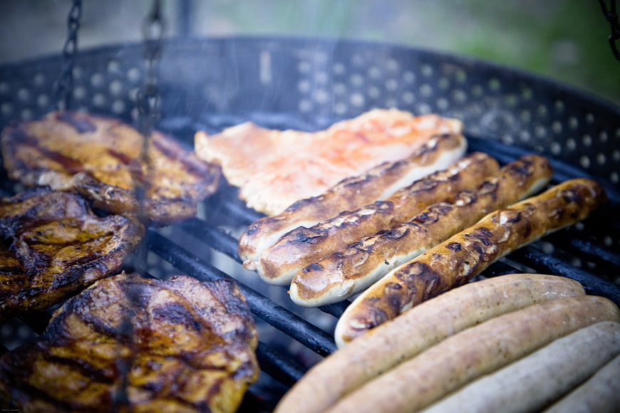 Grilled sausages and steaks on a barbecue grill with smoke