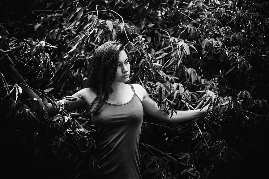 Black and white portrait of a woman standing in dense foliage