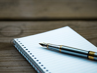 Silver fountain pen on lined notebook on wooden table