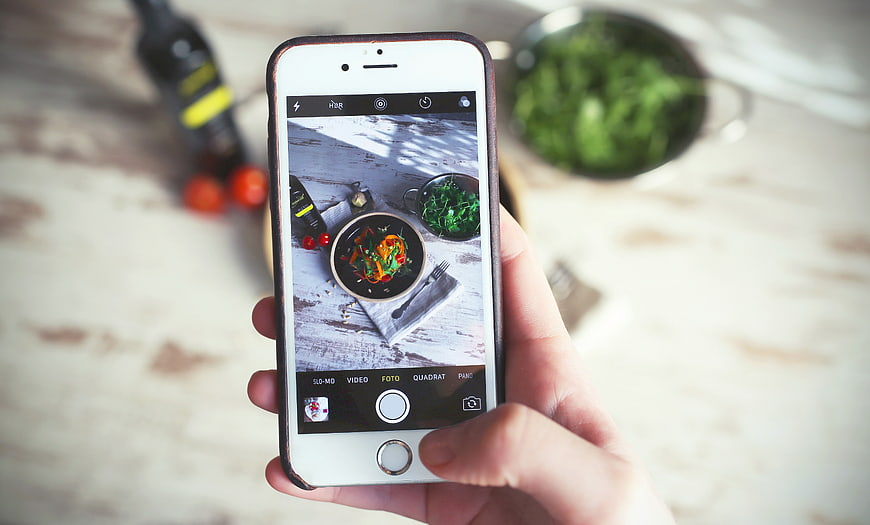 Hand holding smartphone photographing food dish