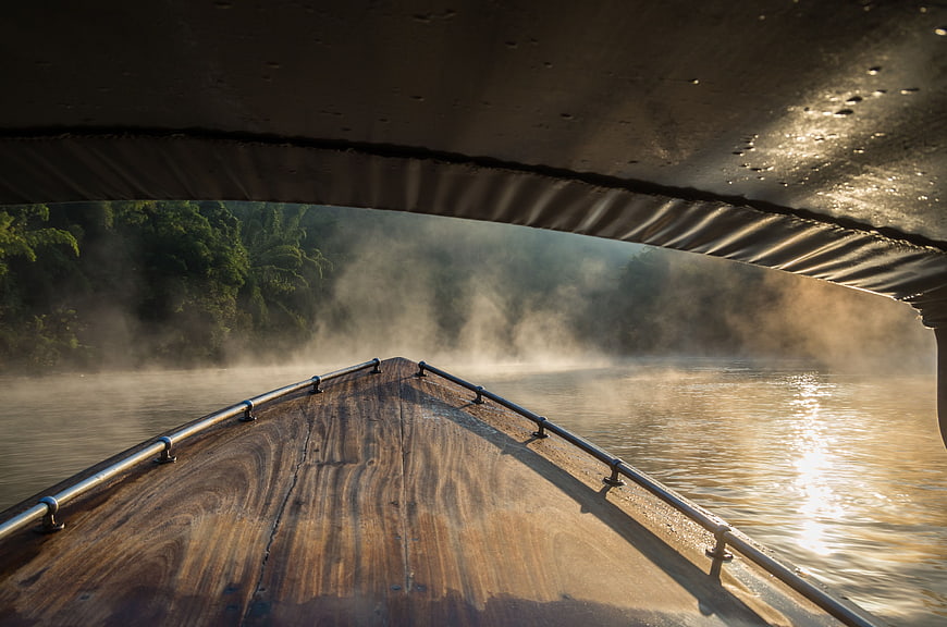 Wooden boat prow on misty river at sunrise