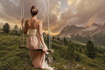 Woman in pink dress on swing in mountain landscape at sunset