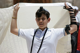 Young Jewish boy wearing tefillin and holding tallit during prayer