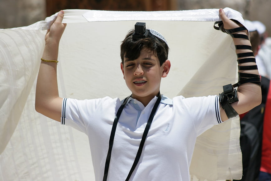 Young Jewish boy wearing tefillin and holding tallit during prayer