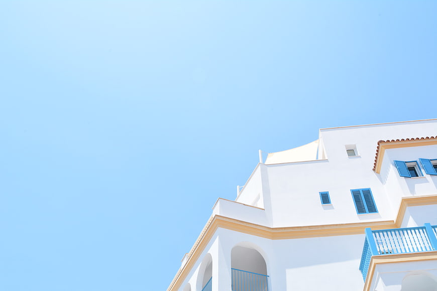 White Mediterranean Building with Blue Shutters Against Clear Sky