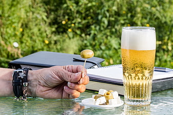 Hand holding olive skewer with beer and feta cheese on outdoor table