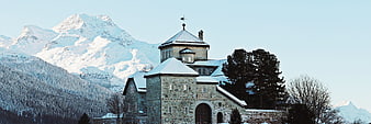 Historic stone church in snowy Swiss Alps with mountain backdrop