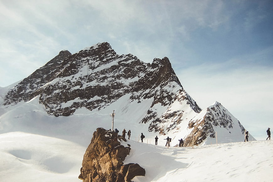 Hikers on Snowy Mountain Ridge with Majestic Peaks