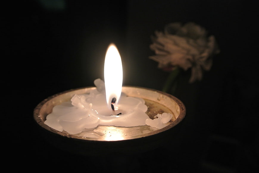 Lit Candle in Metal Holder with Blurred White Flower