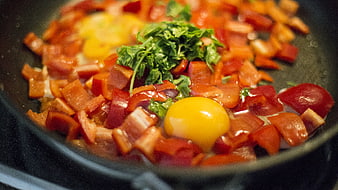 Fresh eggs and chopped red peppers cooking in a frying pan
